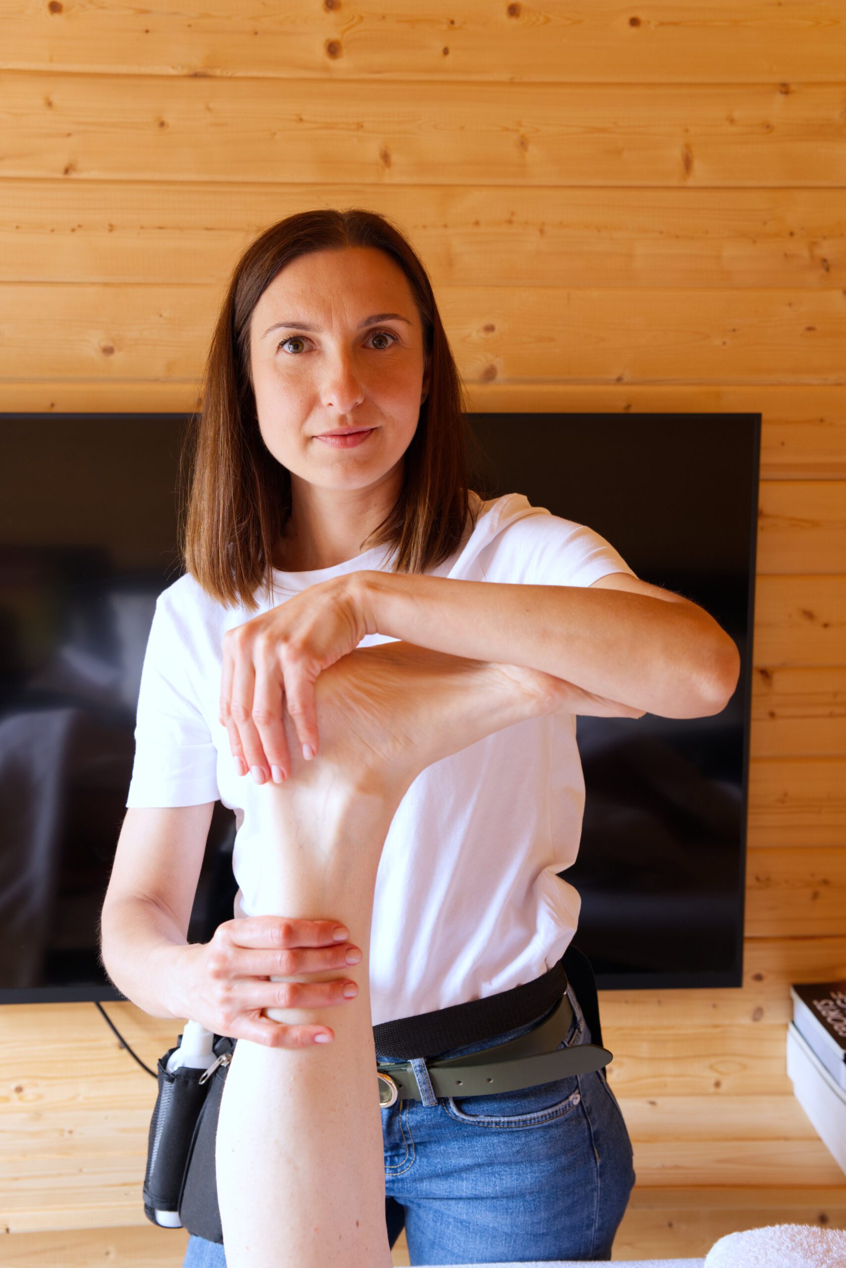 Massage therapist looking straight at the camera, while stretching a customer's leg, during a Kent branding photoshoot